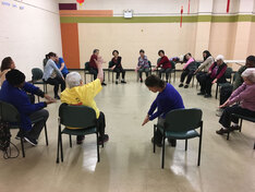 Seniors sit on chairs in a circle  during a movement workshop